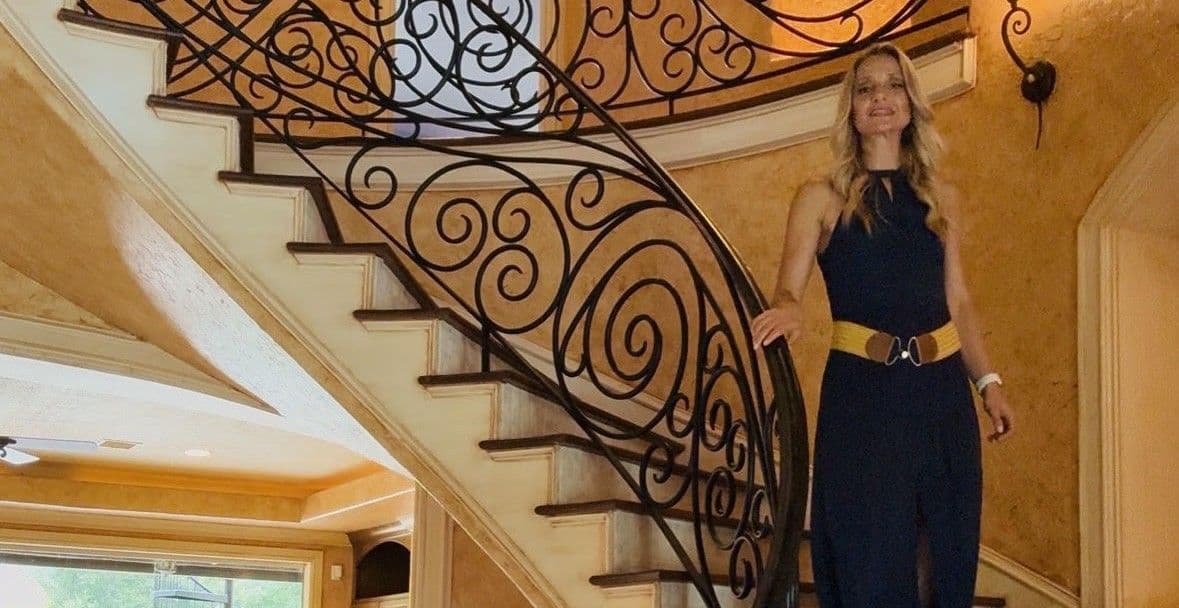Roberta Meggs walking down a curved wrought-iron staircase in a luxury Houston-area home